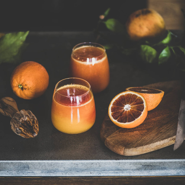 Two glasses of freshly squeezed blood orange juice or smoothie on concrete kitchen counter, square crop. Healthy lifestyle, vegan, vegetarian, alkaline diet, spring detox concept - Fotó, kép
