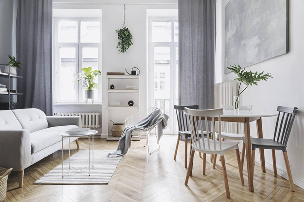 Bright home nordic living room with design sofa, family table, plant, white bookstand on the wall. Brown wooden parquet. Abstract painting on the white wall. Concept of minimalistic interior. - Photo, image