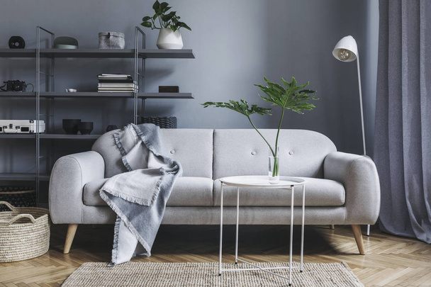 Modern nordic living room with design sofa with elegant blanket, coffee table,white lamp and bookstand on the grey wall. Brown wooden parquet. Concept of minimalistic interior. - Photo, image