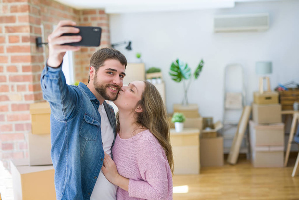 Joven hermosa pareja tomando una foto selfie usando un teléfono inteligente sonriendo muy feliz por mudarse a un nuevo hogar
 - Foto, Imagen