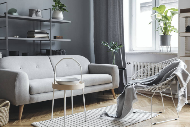 Modern and scandinavian living room with design sofa, coffee table, plants, stylish accessories and bookstand on the grey wall. Brown wooden parquet. Concept of minimalistic and elegant interior. - Foto, Bild