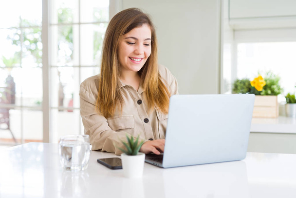 Kaunis nuori nainen, joka käyttää tietokonetta läppäri onnellinen kasvot seisoo ja hymyilee luottavainen hymy osoittaa hampaat
 - Valokuva, kuva