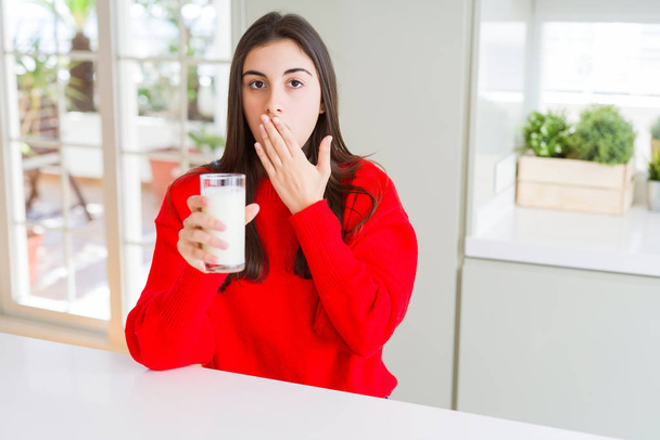 schöne junge Frau trinkt ein Glas frische Milch Deckel Mund mit der Hand schockiert vor Scham für Fehler, Ausdruck der Angst, Angst in der Stille, geheimes Konzept - Foto, Bild