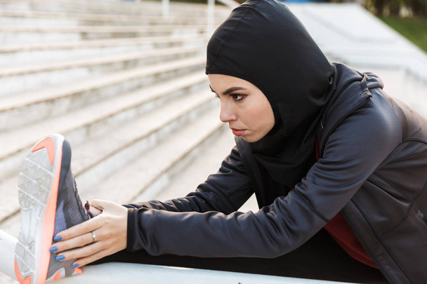 Muslim sports fitness woman dressed in hijab posing make sport stretching exercises outdoors at the street with steps on background. - Φωτογραφία, εικόνα