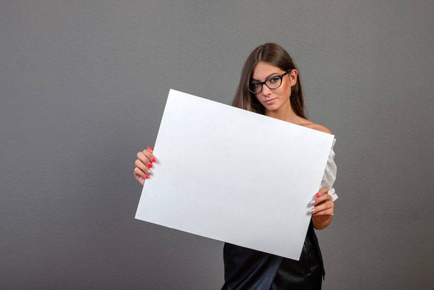 Beautiful woman holding a blank billboard isolated on gray backg - Фото, изображение