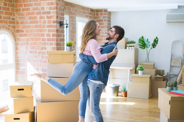 Young beautiful couple in love celebrating moving to a new home around cardboard boxes - Foto, afbeelding