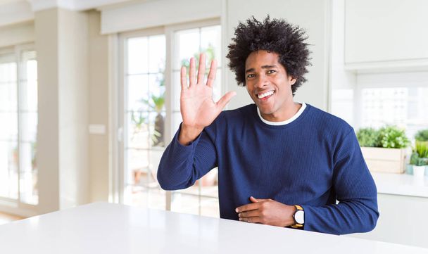 Jeune homme afro-américain portant un pull décontracté assis à la maison Renonçant à dire bonjour heureux et souriant, geste de bienvenue amical
 - Photo, image