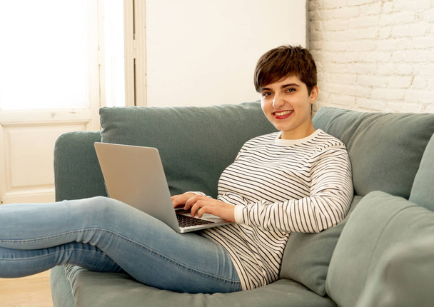 Lifestyle portrait of happy pretty young woman using laptop surfing on the internet and social-media sitting on cosy sofa at home in technology lifestyle communication and people concept. - Фото, изображение