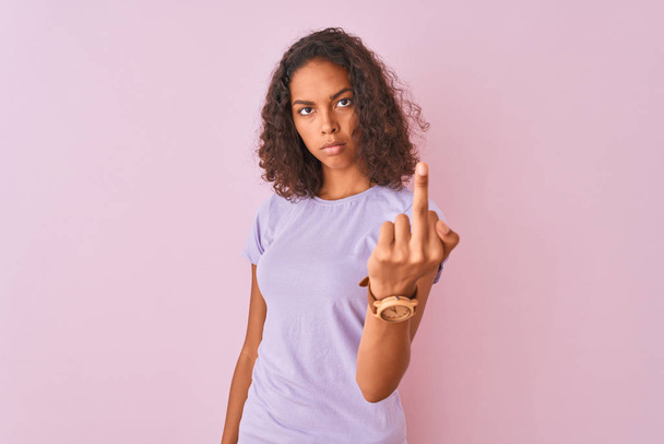 junge Brasilianerin trägt T-Shirt, das über isoliertem rosa Hintergrund steht und Mittelfinger, unhöflichen und unhöflichen Ausdruck zeigt - Foto, Bild