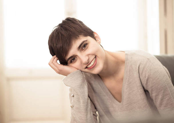 Life style woman indoor portrait of Stunning short haired young woman with beautiful smile sitting on sofa at home with beautiful light. In People youth and leisure concept. - Фото, изображение