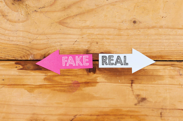 Fake oder echtes Konzept. Fake oder real in Papierpfeilen auf Holzgrund geschrieben. Geschäftskonzept - Foto, Bild