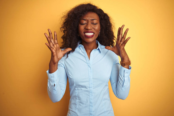 Femme d'affaires afro-américaine portant une chemise élégante sur fond jaune isolé célébrant fou et fou de succès avec les bras levés et les yeux fermés hurlant excités. Concept gagnant
 - Photo, image