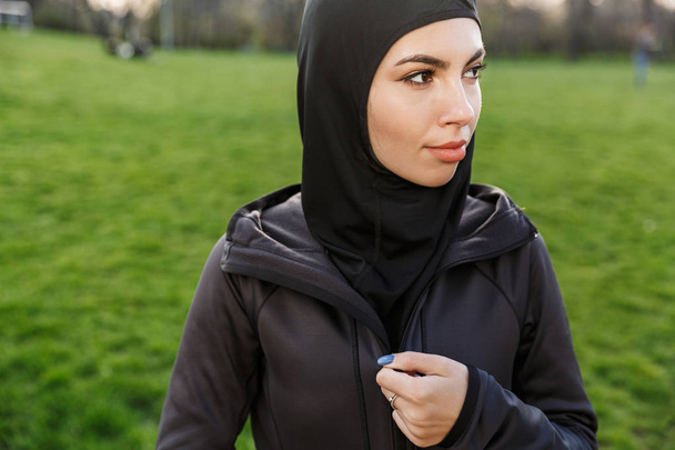 Portrait of attractive athletic muslim woman dressed in religious black hijab walking and doing workout outdoors - Fotografie, Obrázek