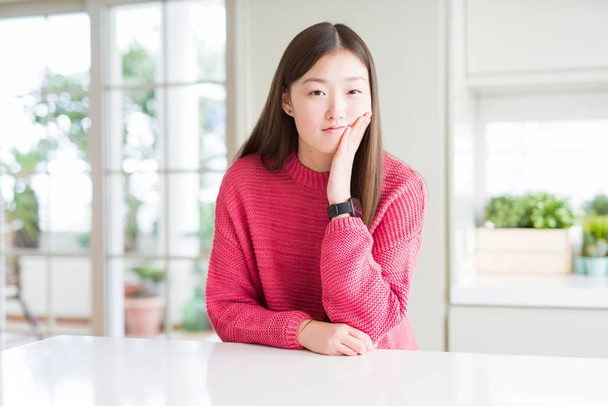 Красива Азіатська жінка носити рожевий светр на білому столі мислення дивлячись втомився і нудно з проблемами депресії схрещеними руками. - Фото, зображення