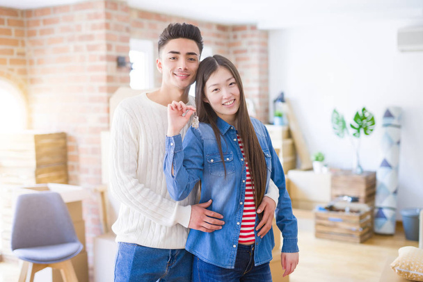 Νεαρό ασιατικό ζευγάρι που κρατά τα κλειδιά του νέου σπιτιού, χαμογελαστός ευτυχισμένος και  - Φωτογραφία, εικόνα