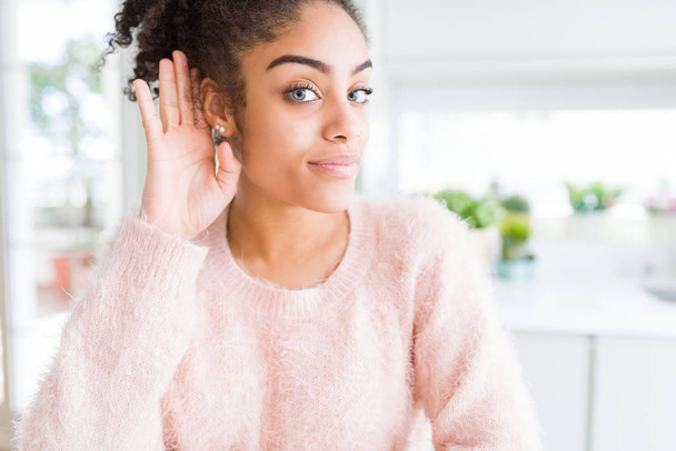 Belle jeune femme afro-américaine aux cheveux afro souriant main sur oreille en écoutant une rumeur ou des commérages. Concept de surdité
. - Photo, image