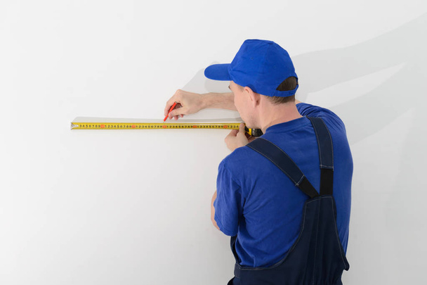 Master builder in uniform of measuring distances on a white wall - Foto, Bild