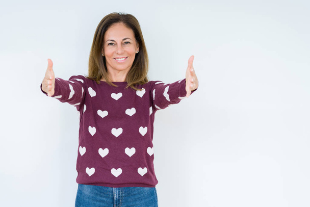 Beautiful middle age woman wearing heart sweater over isolated background looking at the camera smiling with open arms for hug. Cheerful expression embracing happiness. - Zdjęcie, obraz