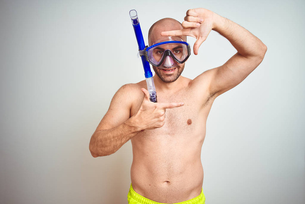 Młody mężczyzna noszenie nurkowanie Snorkel gogle equipent na białym tle uśmiechając się ramki z rąk i palców z szczęśliwą twarzą. Koncepcja kreatywności i fotografii. - Zdjęcie, obraz
