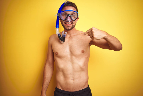 Jovem bonito homem sem camisa vestindo óculos de mergulho sobre fundo amarelo isolado com rosto surpresa apontando o dedo para si mesmo
 - Foto, Imagem
