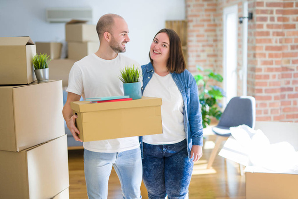 Young couple moving to a new home, smiling happy holding cardboa - Photo, Image