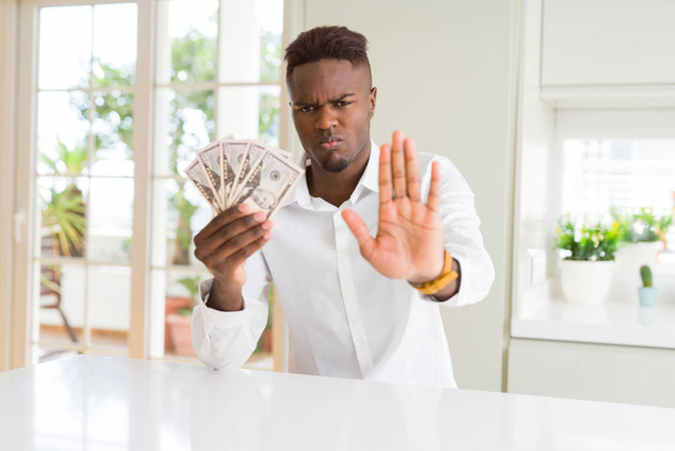 Uomo afroamericano in possesso di banconote da cinquanta dollari a mano aperta facendo stop segno con espressione seria e fiduciosa, gesto di difesa
 - Foto, immagini