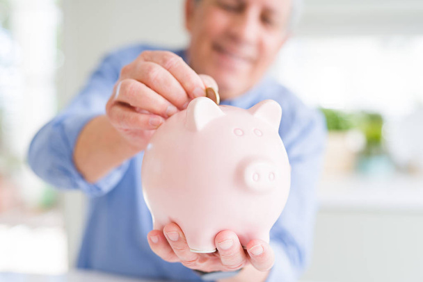 Man brengen een munt binnen piggy bank als besparingen glimlachend vertrouwen - Foto, afbeelding