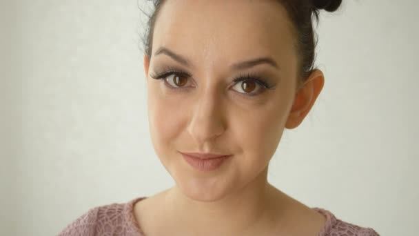 Portrait of a smiling girl with long false eyelashes and brown eyes. Lovely female model with vogue makeup on white background - Filmmaterial, Video
