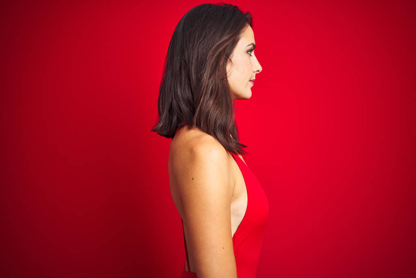 Belle femme portant des maillots de bain bikini sur fond rouge isolé regardant vers le côté, pose de profil relax avec visage naturel avec sourire confiant
. - Photo, image