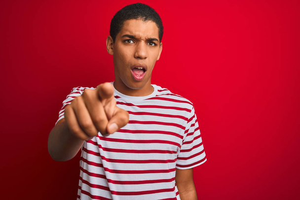 Young handsome arab man wearing striped t-shirt over isolated red background pointing displeased and frustrated to the camera, angry and furious with you - Zdjęcie, obraz