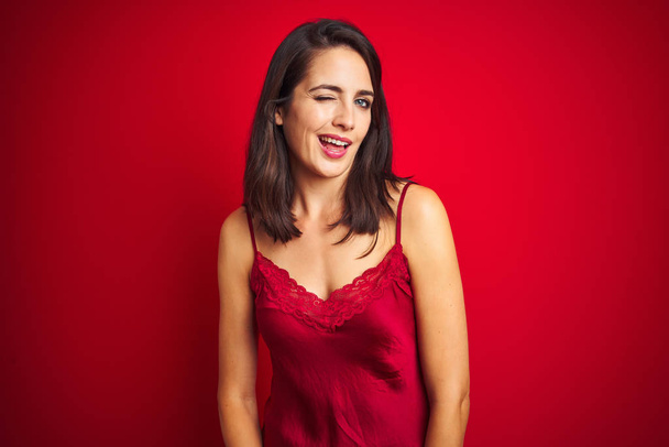 Young beautiful woman wearing sexy lingerie over red isolated background winking looking at the camera with sexy expression, cheerful and happy face. - Foto, Imagen