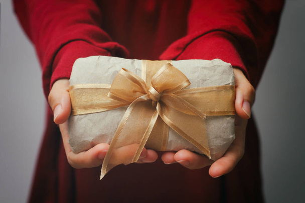 Рука тримає подарункову коробку. Подарунок обгорнутий ремісничим папером та атласною стрічкою. Маленька посилка в руках дівчат. Різдвяний час
.  - Фото, зображення