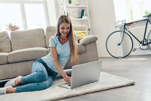 Beautiful young woman smiling and using laptop while resting at home    - Foto, Bild