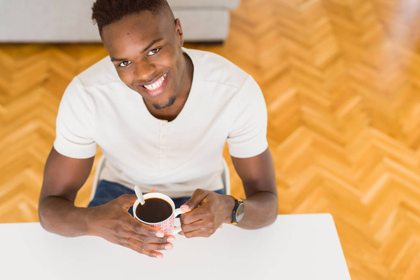 Αφρικανική αμερικανική άνθρωπος που χαμογελά αυτοπεποίθηση πίνοντας ένα καφέ στο σπίτι - Φωτογραφία, εικόνα
