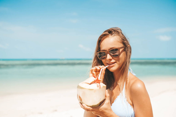 Young beautiful woman drinking coconut water on tropical beach - Фото, изображение