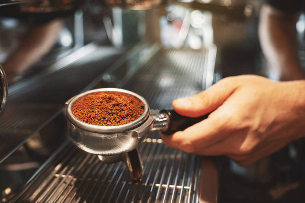 barista holding coffee holder with ground coffee near professional coffee machine preparing coffee drink in cafe close up - Foto, Bild