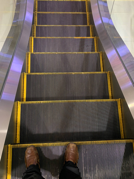 Selfie των ποδιών του ανθρώπου σε καφέ παπούτσια στα σκαλιά των κυλιόμενων κλιμάκων στο αρδ - Φωτογραφία, εικόνα