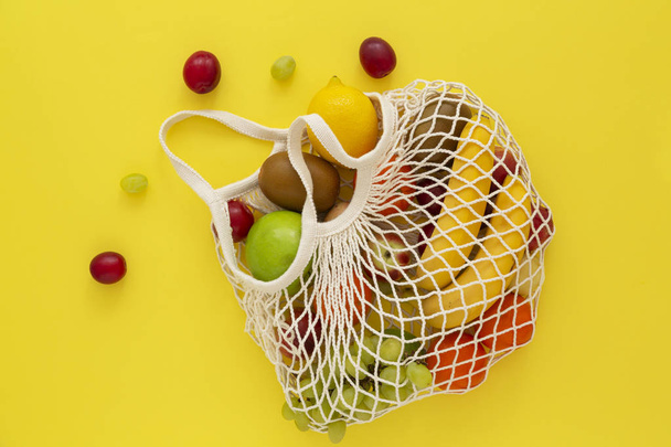 Mesh shopping bag with fruit on pink background. Concept caring for the environment and the rejection of plastic. Reusable net bag or mesh shopper. Healthy clean eating diet and detox. Summer fruits. Flat lay. Top view.  - Photo, Image