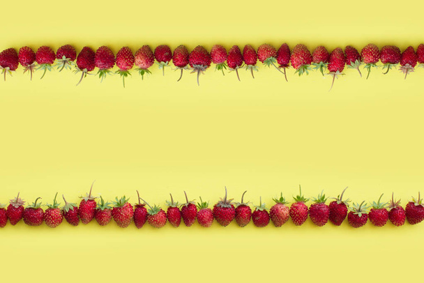 linha de morangos selvagens vermelhos em um fundo amarelo. espaço de cópia. espaço para texto
 - Foto, Imagem