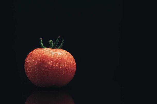 Fresh tomato on a black glass table and dark background. - Photo, Image
