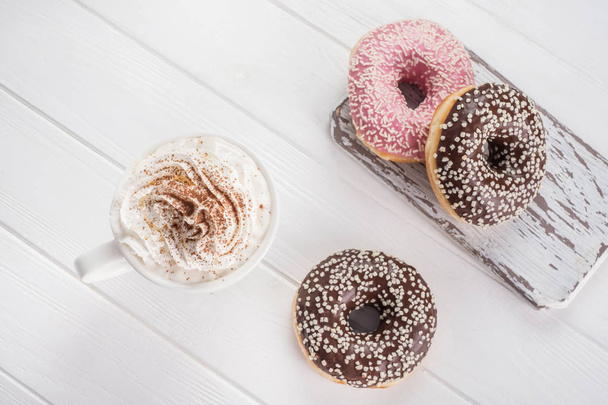 Donuts rosa e chocolate com café com creme na mesa de madeira branca
. - Foto, Imagem