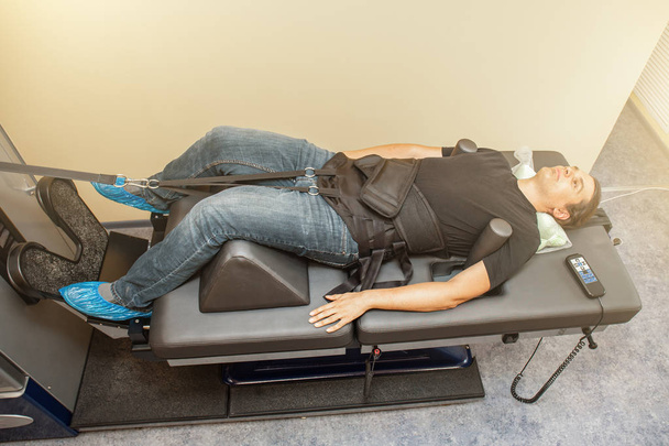 Man on treatment recovery physiotherapy of human spine by stretching with special medical equipment in clinic, orthopedics problems with vertebrae spinal discs - Photo, image