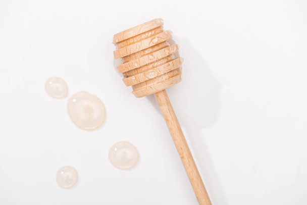 top view of honey drops and wooden honey dipper on white background - Foto, Bild