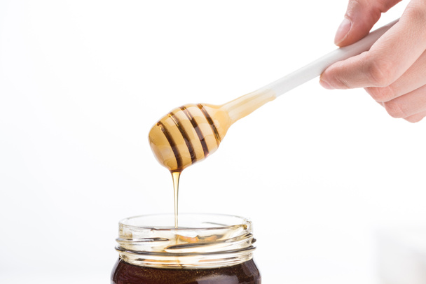 vista parcial del hombre sosteniendo cazo de miel con miel goteando en frasco aislado en blanco
  - Foto, imagen