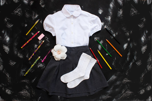 White shirt, grey skirt and stationery supplies on black background. The first of september, new school year. - Photo, Image