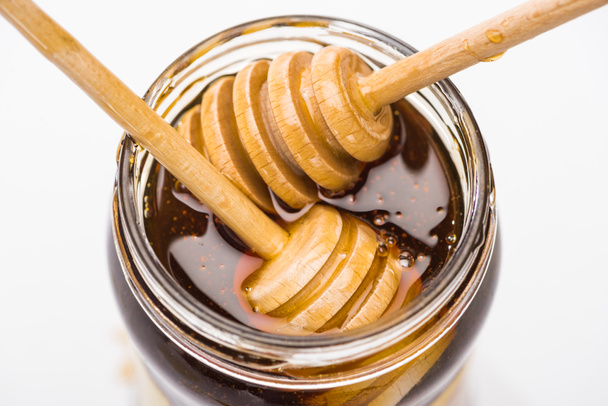 pot met honing en houten honing dippers geïsoleerd op wit  - Foto, afbeelding