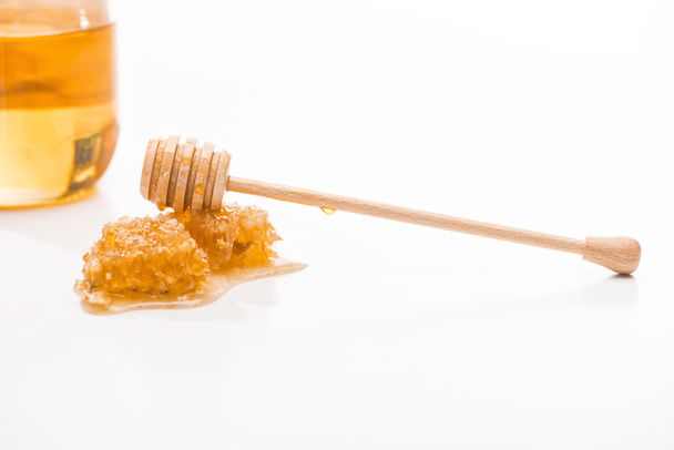 甘い蜂蜜と白に分離された瓶の近くに木製の蜂蜜ディッパーとハニカム - 写真・画像