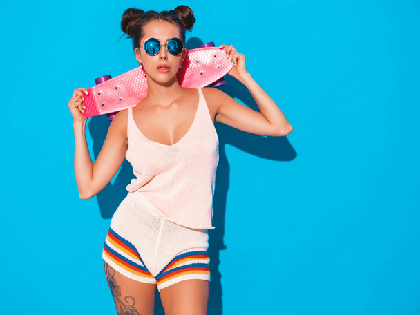 Young beautiful sexy smiling hipster woman in sunglasses.Trendy girl in summer knitted cardigan topic ,shorts.Positive female going crazy with pink penny skateboard,isolated on - Photo, Image