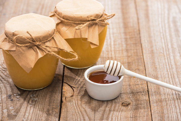 jars with honey near bowl and honey dipper on wooden table - Φωτογραφία, εικόνα