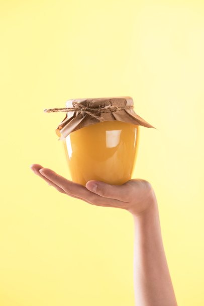 partial view of woman holding glass jar with delicious honey isolated on yellow - Fotó, kép